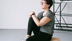 Senior woman in active wear sitting on a wooden box indoors, reflecting on wellness.