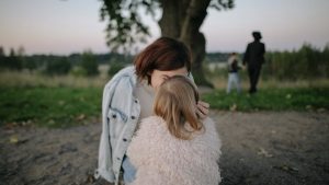 A tender moment between mother and daughter outdoors in a grassy field at twilight.